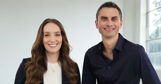 Two smiling individuals standing side by side in a modern office setting.