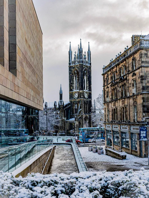 View of Newcastle University's neo-Gothic tower through a snowy street flanked by modern and classical buildings.