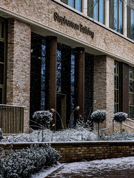 Exterior view of the Stephenson Building with light snowfall, featuring snow-covered bushes and bare trees in the foreground.
