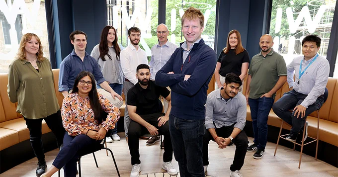 Group of ten professionals smiling at the camera, standing in a modern office environment.