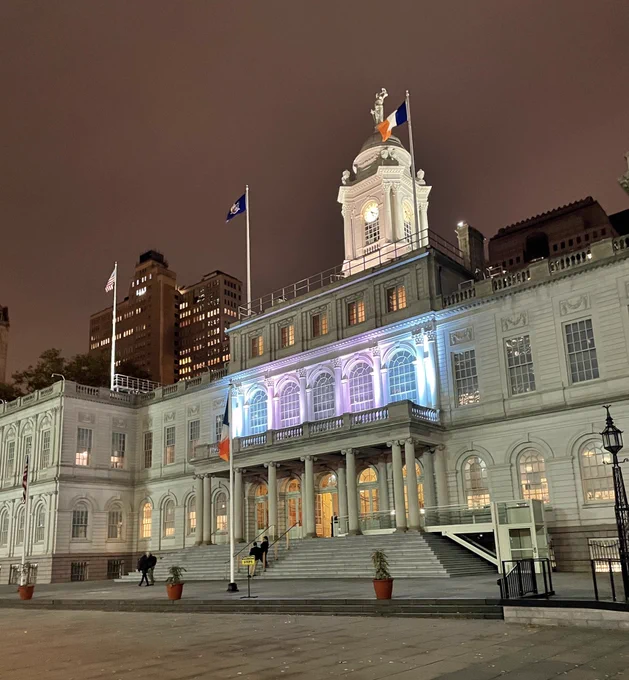 City Hall lit up in pink, white, and blue on a cloudy night